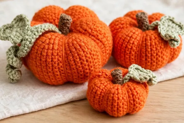 A large crocheted orange pumpkin with a brown stem, a sage green leaf and a curly vine, on a wooden table