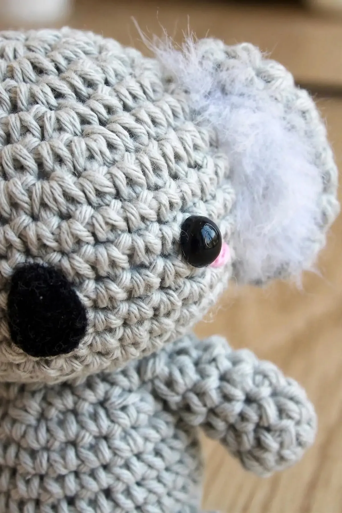 A close-up of the crocheted koala’s face, showing its black felt nose, safety eye and fluffy white ear
