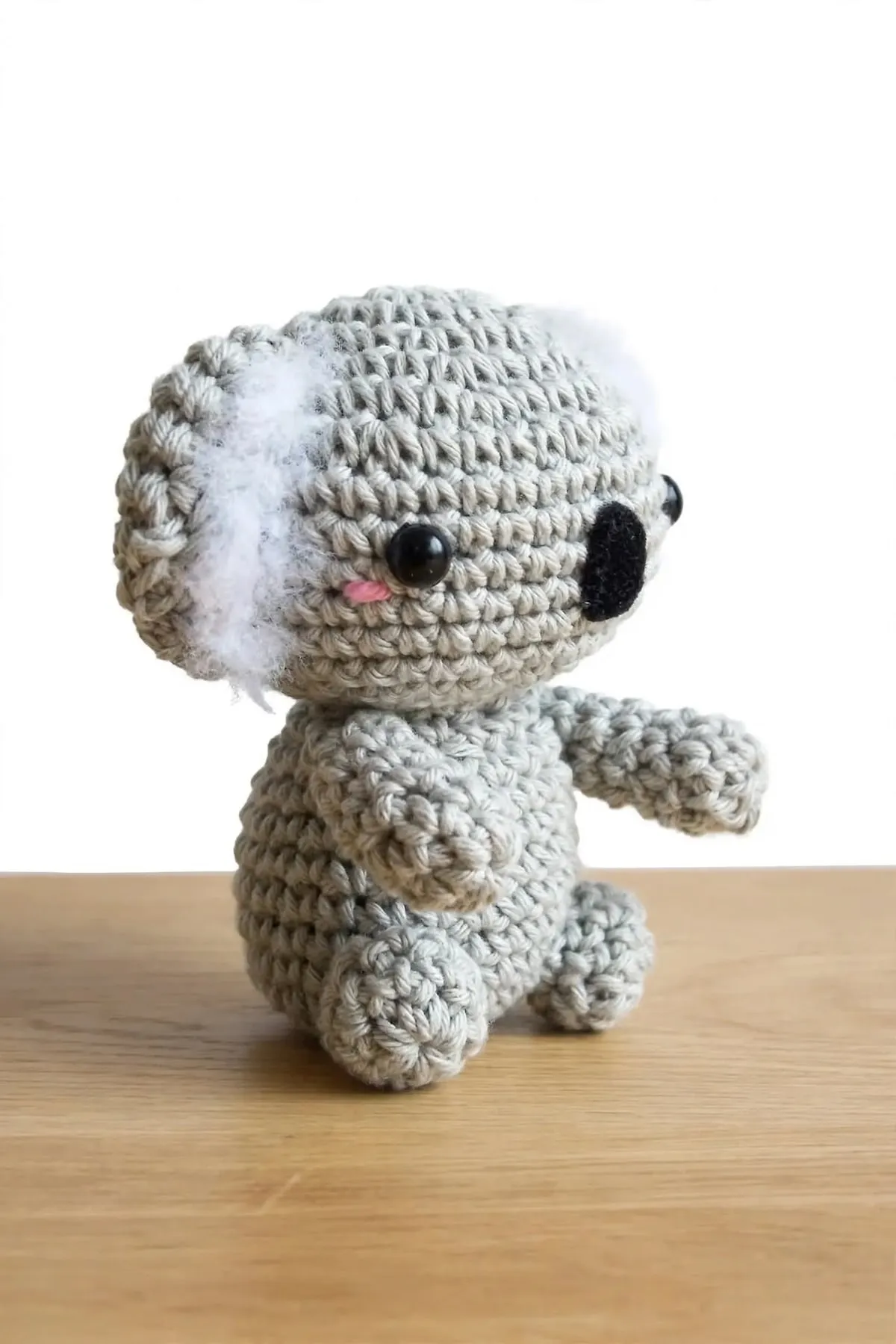 The crocheted mini koala seen from the side, showing its round body, arm and fluffy ear
