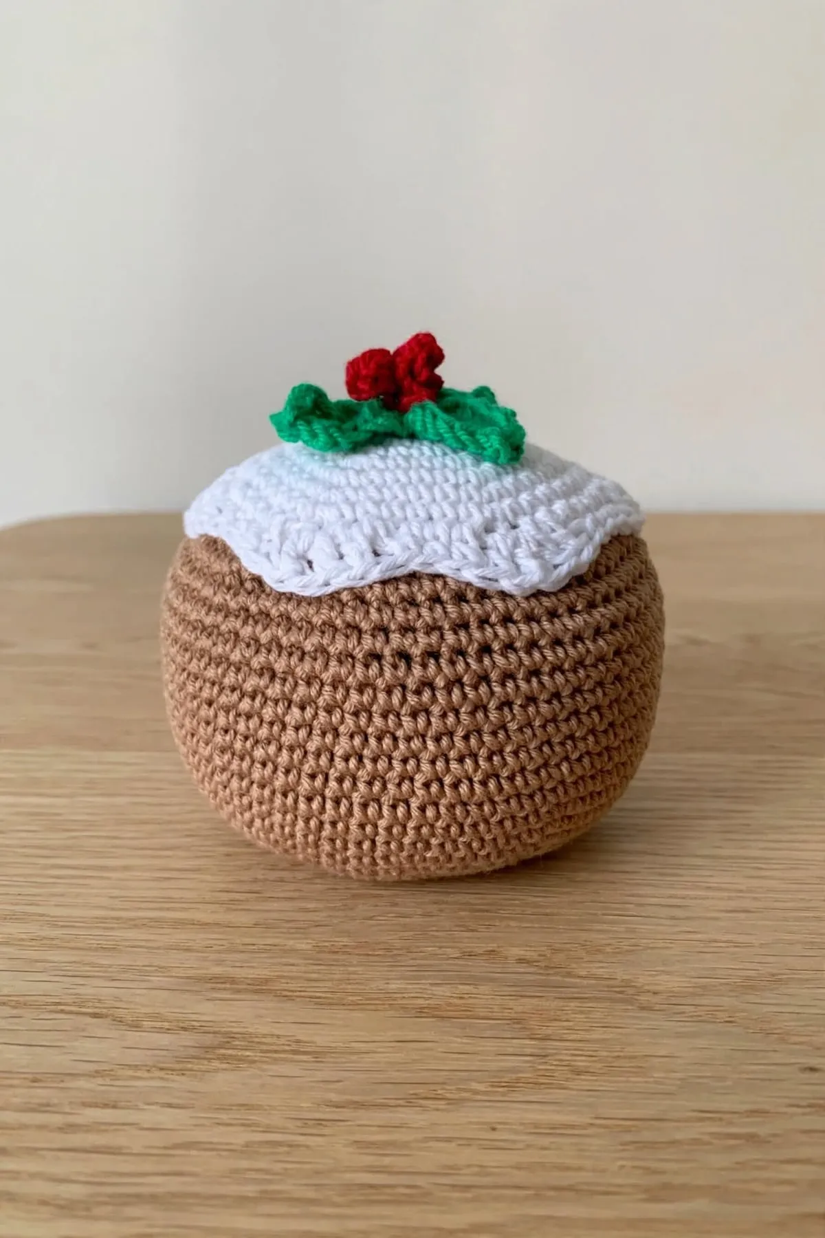 The crocheted Christmas pudding from the side, showing the scalloped white icing over the round brown body