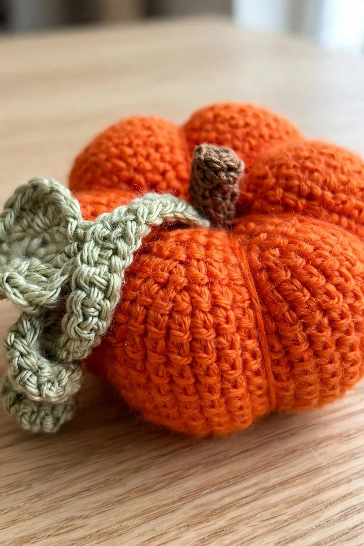 A close-up of a crocheted pumpkin’s stitches, stem and curly leaf